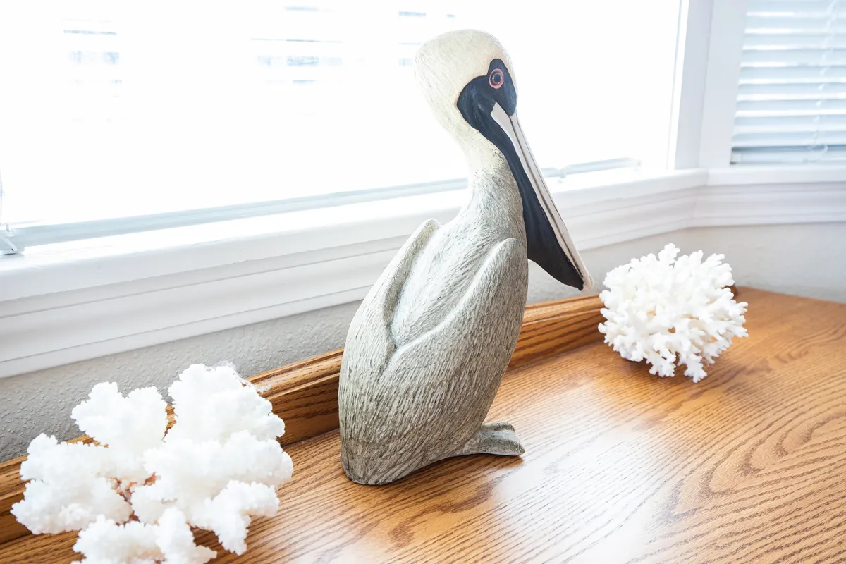 A peaceful corner adorned with a wooden pelican figurine and white coral decorations, sunlight streaming through the window. The setting invites quiet moments, perhaps reading or casually conversing, evoking a sense of tranquility and connection to the lake's natural beauty.