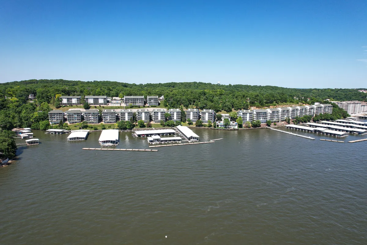 An expansive view of the lakefront condominiums, marina with boat docks, and lush greenery. The scene captures both the tranquil waters and the interconnectedness of boardwalks and dock spaces.