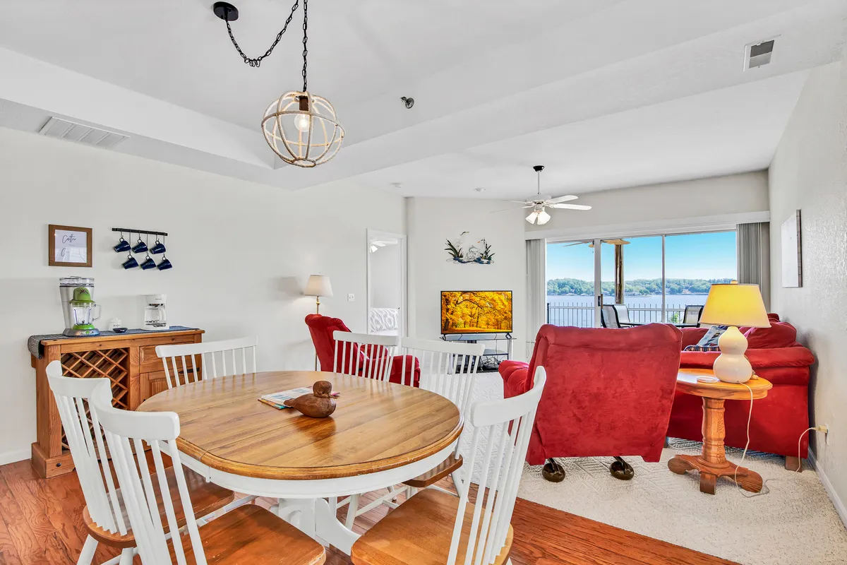 A spacious interior living area featuring a round wooden dining table, plush red sofas, and a large window that offers views out to the exterior. The setup suggests a comfortable space for gathering, with the window hinting at the scenic vistas beyond—potentially where guests could watch the Lake Race and fireworks from inside.