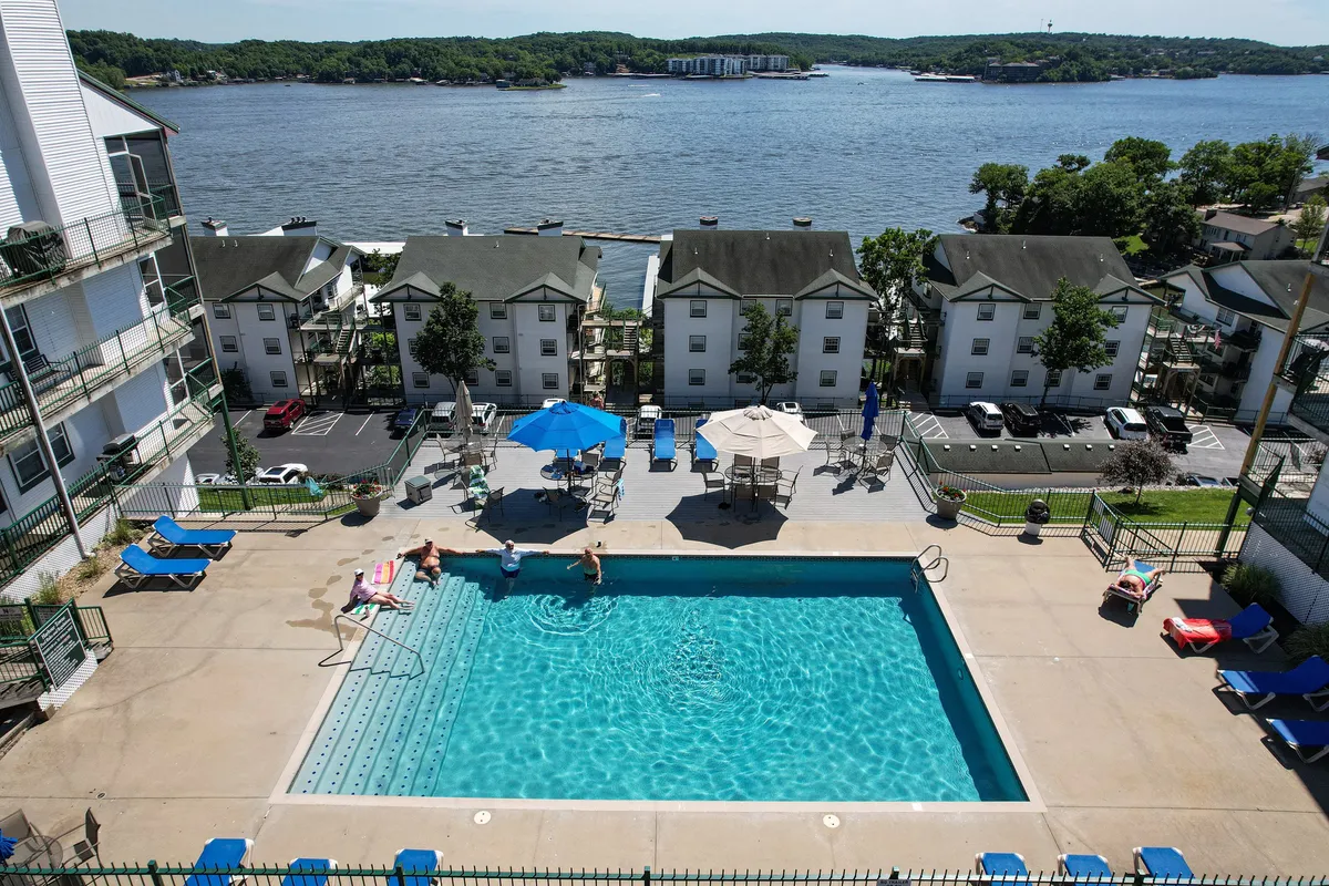 A waterfront swimming pool area lined with lounge chairs and umbrellas, all positioned to take in the lake view just beyond. The inviting pool space is ideal for leisurely swims, sunbathing, or socializing with others, with sunset hues visible from this vantage point.
