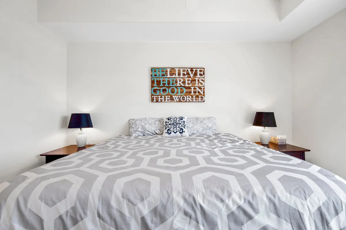 A cozy bed with patterned bedding and table lamps rests against soft-colored walls adorned with motivational art. The lighting and arrangement create a calming, inviting environment perfect for unwinding after a day of lake adventures.